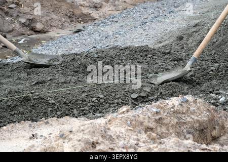 Two shovels mix gray concrete on a construction site under cloudy skies. Stock Photo