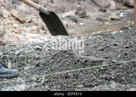 A worker mixes and spreads new concrete on a construction site while using a shovel. Stock Photo