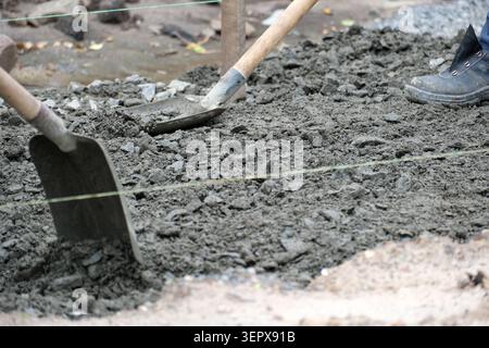 Laborers skillfully prepare wet concrete, shaping it for a sturdy walkway surface. Stock Photo