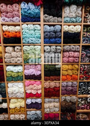 Collection of colorful yarn skeins arranged on wooden shelves in a craft store. Knitting, handmade products and creative hobby concept. Stock Photo