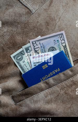 Passport boarding pass and US dollars in a jacket pocket. Close up of blue passport boarding pass and dollar banknotes inside a brown suede pocket, tr Stock Photo