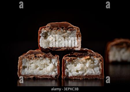 Stack of milk chocolate bars cut in half with coconut filling, close up. Macro shot of broken chocolate bars with white coconut flakes inside stacked Stock Photo