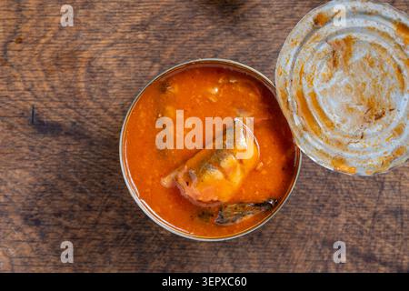 Open tin can of sardines in tomato sauce on wooden background, close up. Top view of opened canned fish sprats or sardines in orange tomato sauce on a Stock Photo