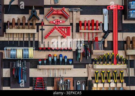 Various old work tools hang on the wooden wall in a home carpentry workshop, close up. Wall French cleat system to hang work tools Stock Photo