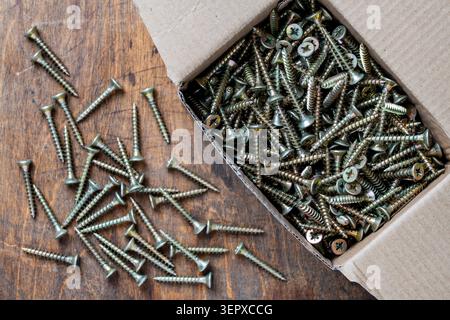 Many golden metal self tapping screws for construction work in a cardboard box on wooden background , close up, top view, copy space. New fasteners se Stock Photo