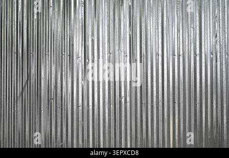 Close up of shiny silver aluminum corrugated panel wall surface with vertical ridges, dents, scuffs, misaligned screws, nail holes Stock Photo