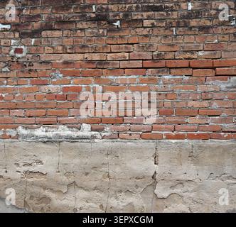 Horizontal close up of a multi surface wall with weathered red bricks, cracked uneven mortar, black smudges, and crumbling concrete Stock Photo