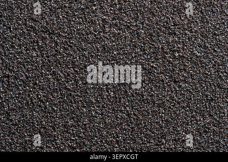 A high-resolution full-frame macro photograph of a dark, coarse, and grainy abrasive texture, resembling sandpaper or a rough stone surface. Ideal for Stock Photo