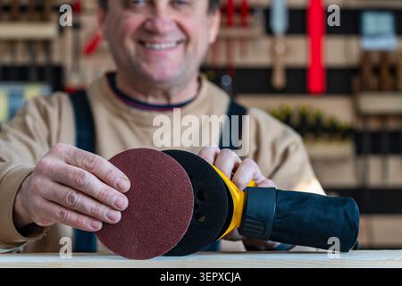Male carpenter in a carpentry workshop fixing an sandpaper on a orbital wood sander for wood floor renovation, close up. Seasonal house chores, woodwo Stock Photo