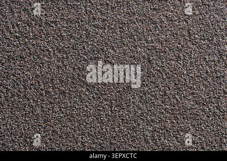 A high-resolution full-frame macro photograph of a dark, coarse, and grainy abrasive texture, resembling sandpaper or a rough stone surface. Ideal for Stock Photo