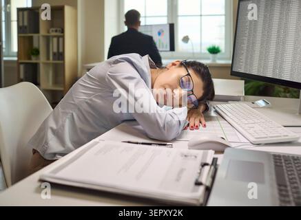 Exhausted office employee woman sleeping at desk with computer and paperwork Stock Photo