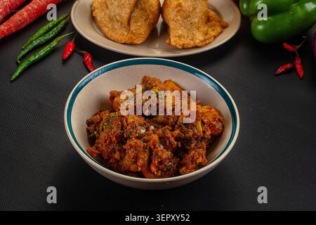 Spicy cauliflower curry served in ceramic bowl with golden fried bread fresh vegetables on dark textured surface. Vibrant orange green colors highligh Stock Photo