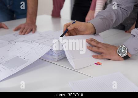 A detailed shot focusing on the hands of an engineer or architect using a pen to point at specific details in a thick binder of technical project docu Stock Photo