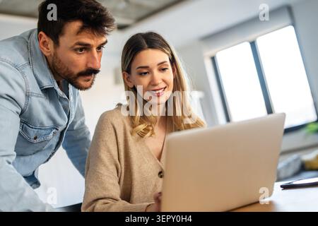 Young happy multiethnic couple having fun while using laptop, digital device at home Stock Photo