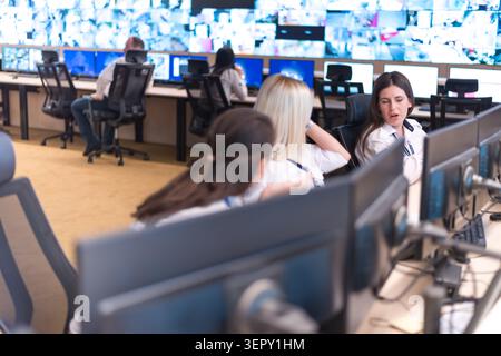 A wide shot of a modern security operations center (SOC) showing multiple operators at workstations monitoring a massive wall of digital surveillance Stock Photo
