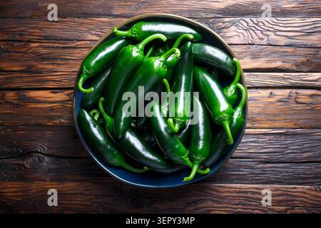 Top view bowl of jalapeno peppers on dark wooden table background. Fresh chili vegetables with rustic texture and natural lighting Stock Photo