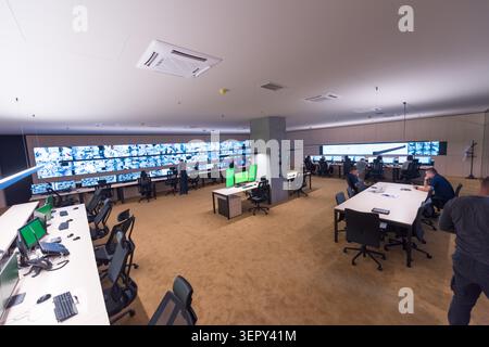 Wide-angle interior view of a high-tech corporate security monitoring center, featuring an expansive video wall displaying multiple surveillance feeds Stock Photo