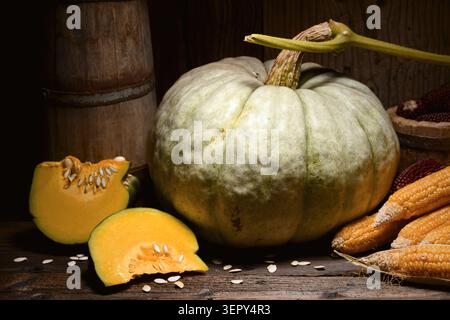 Large pumpkin with sliced pieces on wooden table in dark moody lighting. Autumn composition with squash and rustic seasonal vegetables Stock Photo