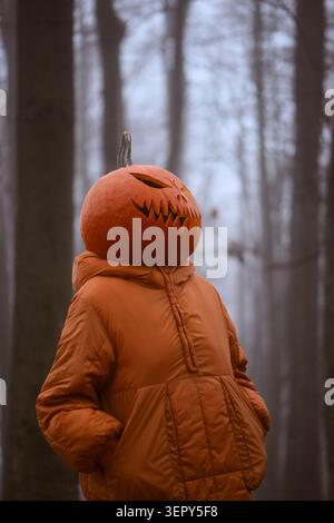 Close up portrait of a mysterious figure with a jack o lantern head wearing an orange jacket. Creative Halloween costume in a foggy woodland setting with cinematic mood Stock Photo