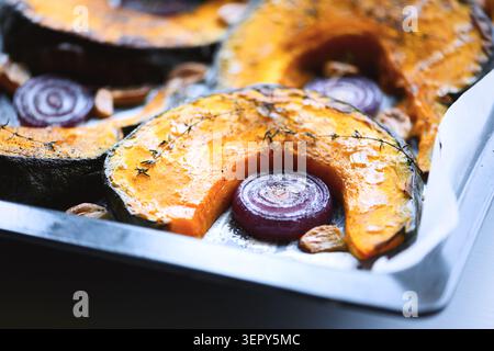 Baked pumpkin slices and red onion arranged in roasting pan. Seasonal comfort food with squash and rustic kitchen styling Stock Photo