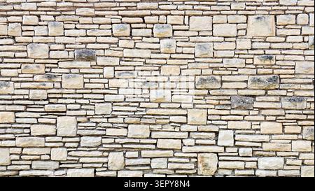 Close-up of a beige natural stone wall with various shapes and sizes of stones arranged in a pattern, showing texture and color variation. Ideal for a Stock Photo