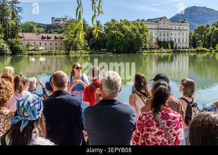 Tour guide Stephanie Hinterbuchner is explaining the area around the Leopoldskron Pond to a group; in the background are Leopoldskron Palace and Hohensalzburg Fortress. The Baroque palace served as the outdoor setting for the Trapp family’s estate in the film ‘The Sound of Music’ (1965). Salzburg, Austria Stock Photo