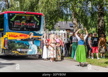 Tour guide Stephanie Hinterbuchner in a dirndl cheers on the tour group with her fist raised in front of the rear of a Panorama Tours coach on Fürstenweg, near Leopoldskron Castle in Salzburg; the coach bears the inscription ‘The Original Sound of Music Tour’. Salzburg Panorama Tours is the officially licensed operator of this city tour of the film locations from *The Sound of Music* (1965). Salzburg, Austria Stock Photo