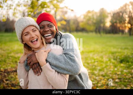 Two happy women friends hugging and laughing outdoors, enjoying a moment of togetherness Stock Photo