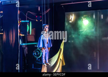 A marionette in an ancient Egyptian-style blue costume, complete with a headdress and chest ornament, hangs from strings on the stage of the Salzburg Marionette Theatre, with stage machinery and spotlights in the background. The figure is part of the theatre’s production of Mozart’s *The Magic Flute*, which is part of its repertoire. Schwarzstraße 24, Salzburg, Austria Stock Photo