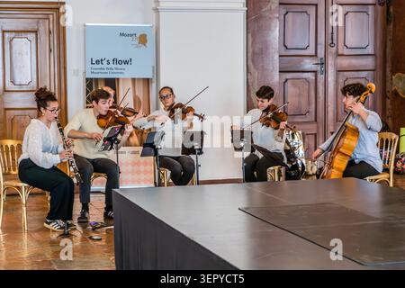 The Bella Musica Ensemble from the Mozarteum University in Salzburg, performing with its full line-up: clarinet, three violins and cello; behind them, the roll-up banner reading ‘Mozart 270 / Let’s flow! / Ensemble Bella Musica / Mozarteum University’. DomQuartier, Salzburg, Austria Stock Photo