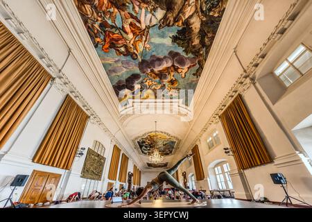 The Baroque ceiling fresco in the ballroom of the Archiepiscopal Residence (DomQuartier Salzburg) dominates the scene; in the foreground, a yoga instructor demonstrates a standing pose, whilst behind her the participants practise on mats. The hall is one of the stately reception rooms of the former residence of the Archbishops of Salzburg. Salzburg, Austria Stock Photo