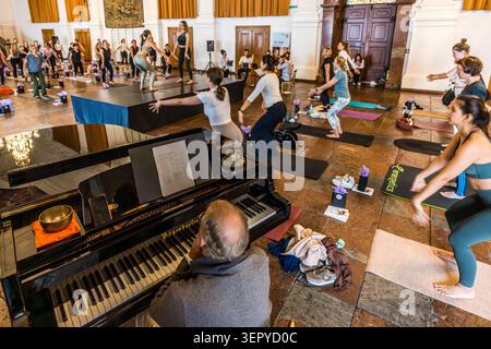Stefan David Hummel at the grand piano in the ballroom of the Archbishop’s Residence (DomQuartier Salzburg); on the piano stands a singing bowl, which is used during the meditation part of the event. In the background, yoga instructors on the podium demonstrate exercises, which the participants follow. Event: ‘Pop Up Yoga – Mozart Edition’. Salzburg, Austria Stock Photo