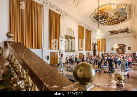A view from the grand Baroque staircase of the Archbishop’s Residence down onto the yoga group in the ballroom: the participants are stretching their arms upwards, with the golden ball-shaped finials of the banister in the foreground. The ballroom is the venue for the ‘Pop Up Yoga – Mozart Edition’ event at the DomQuartier in Salzburg, Austria Stock Photo
