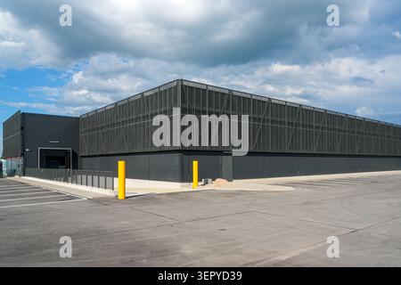 Contemporary logistics and warehouse facility with metal mesh facade, parking spaces and storm clouds overhead Stock Photo