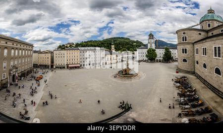 A panoramic view across Residenzplatz in Salzburg, with the Residenzbrunnen (1661) in the centre of the square – one of the largest Baroque fountains north of the Alps. Several horse-drawn carriages are lined up along the right-hand edge of the square; the domes of Salzburg Cathedral rise above the right-hand edge of the picture. The square is a central feature of the Salzburg Old Town ensemble, which was designated a UNESCO World Heritage Site in 1996. Residenzplatz, Salzburg, Austria Stock Photo