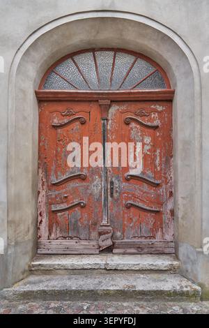 Old weathered wooden door with transom window in a semicircular stone portal Stock Photo