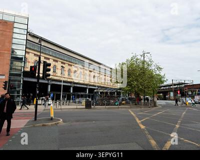 Manchester, UK - May 07, 2026: Busy urban scene at Manchester, UK train station with commuters, crosswalks, vehicles and historic architecture. Stock Photo