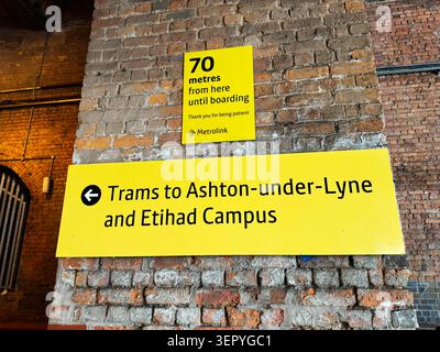 Manchester, UK - May 07, 2026: Bright yellow directional signs on a brick pillar pointing to trams and Etihad Campus in Manchester Stock Photo