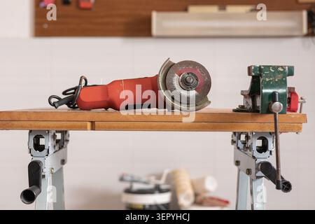 Angle grinder and vise resting on a workbench, depicting professional or hobbyist metalwork, fabrication, and repair tasks Stock Photo