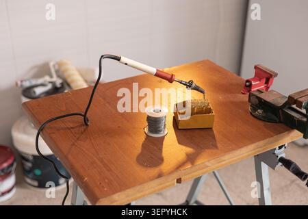 Soldering iron and solder wire positioned on a wooden workbench, ready for electronics repair, DIY projects, or hobby work Stock Photo