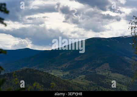 Impressionistic mountain landscape featuring dark, heavy storm clouds hanging low over a vast forested mountain ridge in the Carpathian national park. Stock Photo