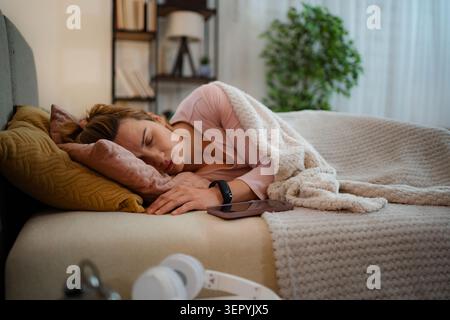 Young adult woman resting comfortably in bed with a wearable activity tracker on her wrist Stock Photo