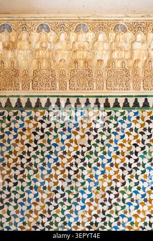 Intricate Arabic carved stucco decoration and colorful geometric ceramic tiles on a historic wall at the Alhambra palace complex in Granada, Spain Stock Photo