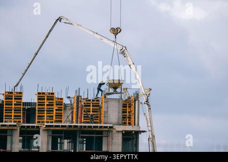 Workers are busy constructing a new high rise residential building, carefully placing concrete into formwork with a crane and concrete pump, symbolizing urban growth and development Stock Photo