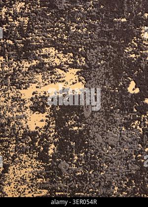 Close-up of heavily weathered dark paint peeling and flaking to expose a beige underlayer. The image shows rough granular paint chips, raised blistere Stock Photo