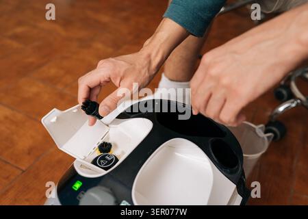 Close-up cropped shot of unrecognizable man replacing brush head on steam cleaner, preparing device for household chores and maintaining proper Stock Photo