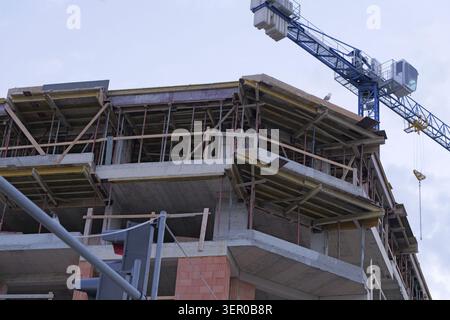 Construction site with an incomplete concrete and brick high rise building under development, featuring wooden formwork for the next floor and a large Stock Photo