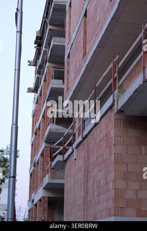 Multi story building under construction with exposed concrete slabs, forming balconies and floors, alongside red hollow brick walls, indicating ongoin Stock Photo