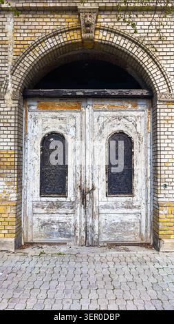 Old distressed entrance door with decorative iron windows and brick facade, historic building detail, vertical image Stock Photo