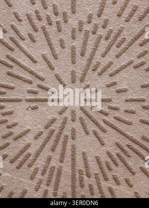 Close-up of a beige textured surface featuring an embossed starburst pattern with raised linear ridges and short dashes radiating from a central point Stock Photo